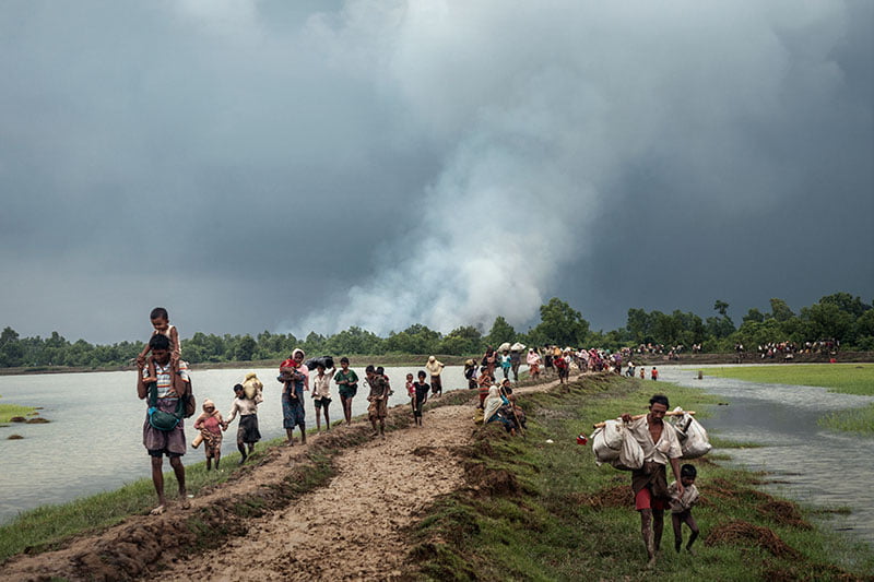 Rohingya refugees stream into Bangladesh after crossing the Naf River, which separates Myanmar and Bangladesh, in September 2017. In the background, smoke rises from villages being burned in northern Rakhine State, Myanmar.