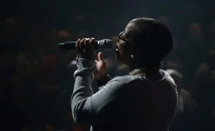 A woman singing into a microphone on stage with a crowd around her