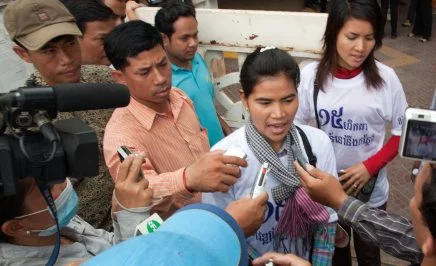 A woman giving an interview, surrounded by journalists with cameras and smartphones