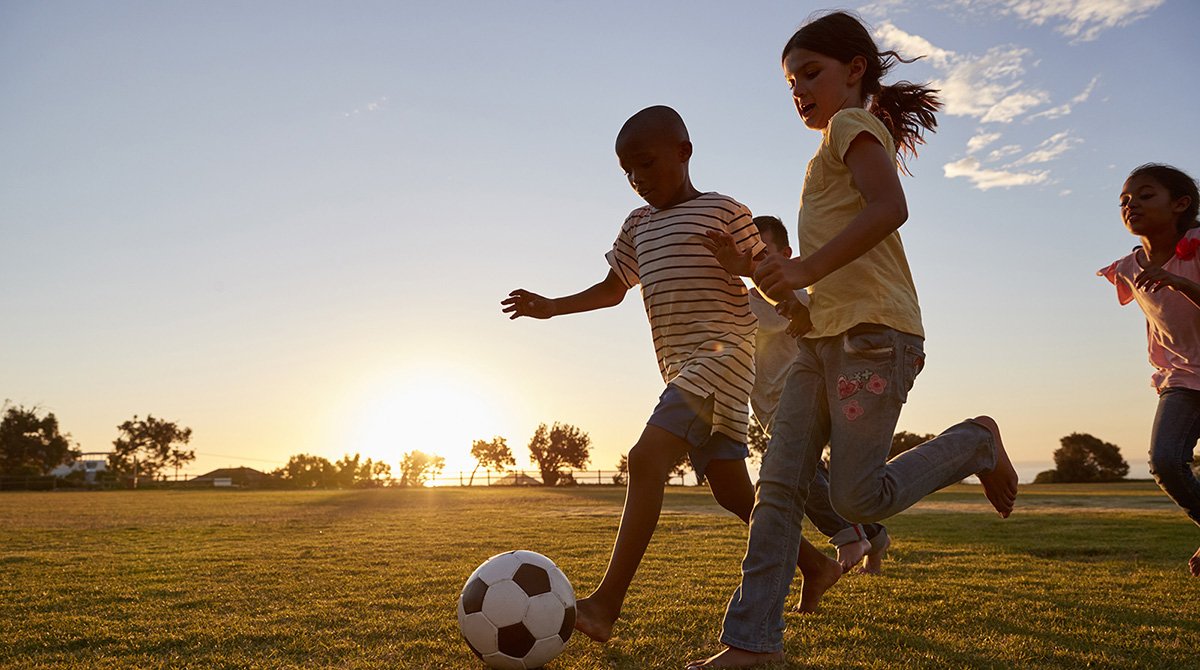 Children racing after a football playing on a field.