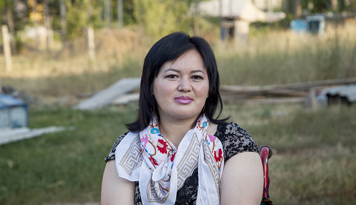 I woman wearing a scarf sits in a wheelchair and stares at the camera.