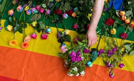 An arm reaching over a rainbow flag to lay rainbow coloured roses on the flag