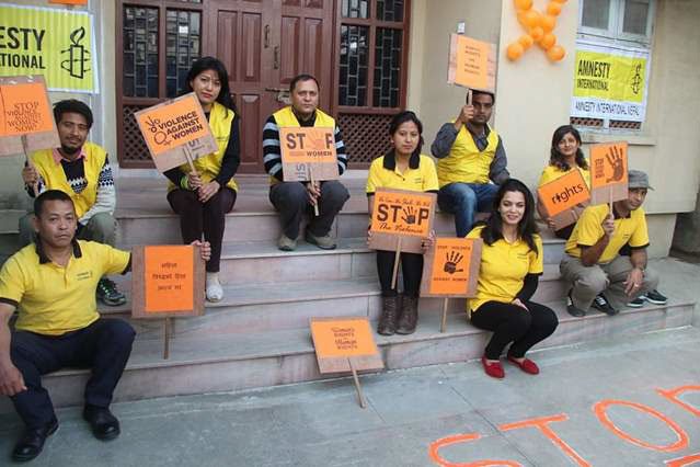 A group of people wearing yellow t-shirts and holding signs that say 'Stop violence against women'.