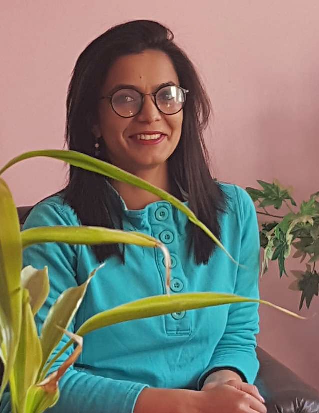 A woman wearing glasses and a blue sweater smiles to the camera.