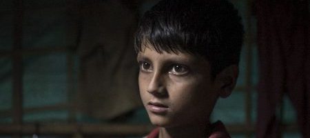 A young Rohingya boy holds a school book in a refugee camp in Bangladesh.