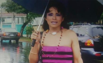 Alejandra, a transgender woman and activist from El Salvador stands in the street with an umbrella.