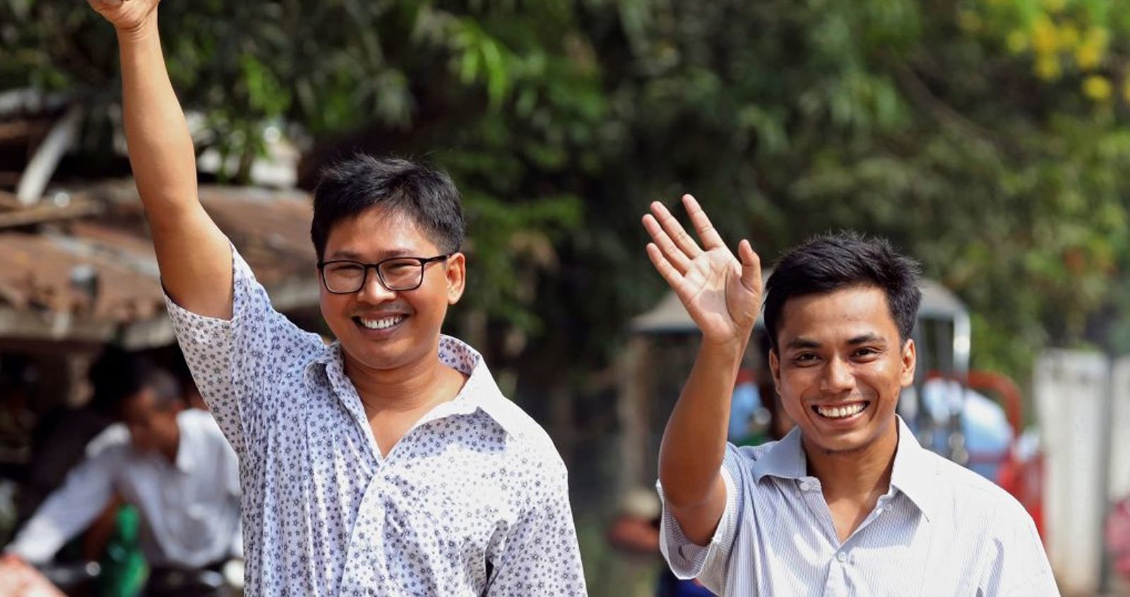 Wa Lone and Kyaw Soe Oo smile widely and wave. Wa Lone has his hand raised in the air in a thumbs up.
