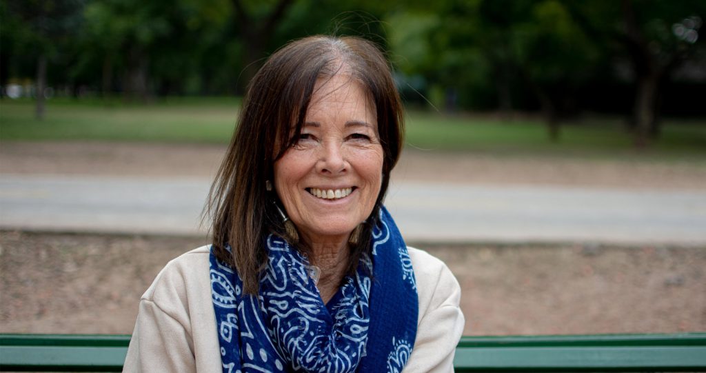 A middle aged woman with shoulder length brown hair on a park bench, smiling