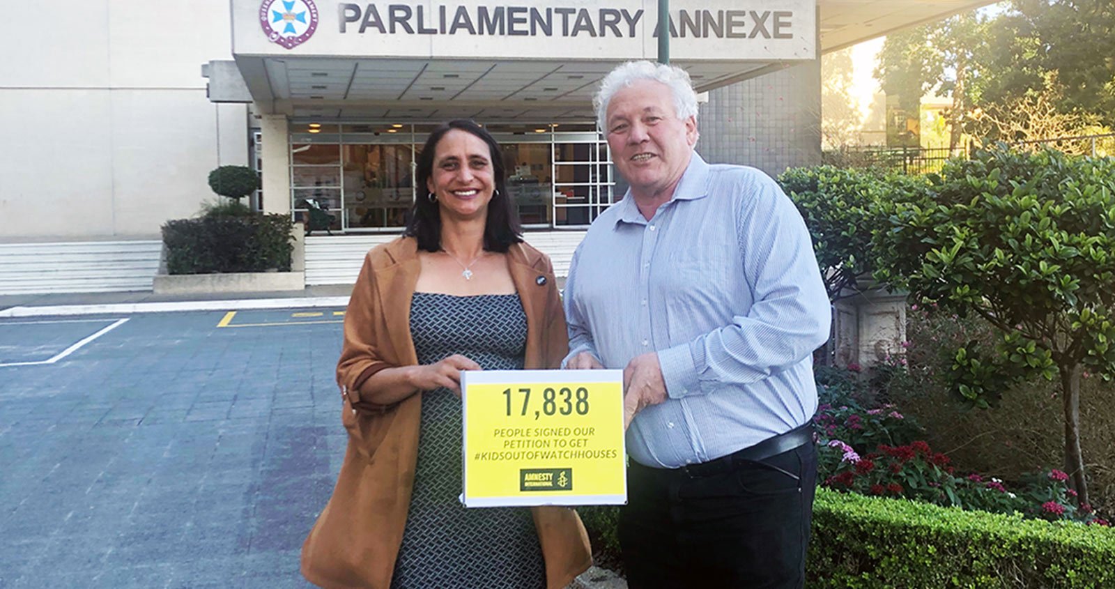 A man and a woman hold a yellox box with a sign on it reading: 17,838 people signed to get kids out of watch houses