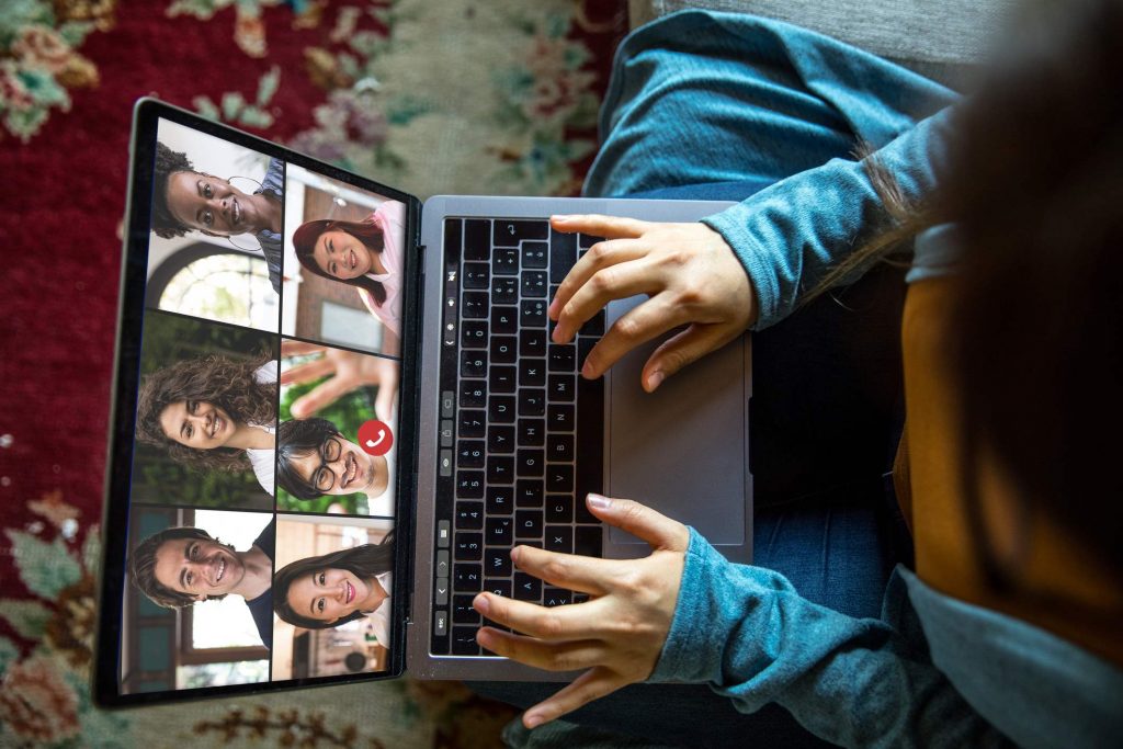 A person types on a laptop, the screen depicts a video call with multiple callers.