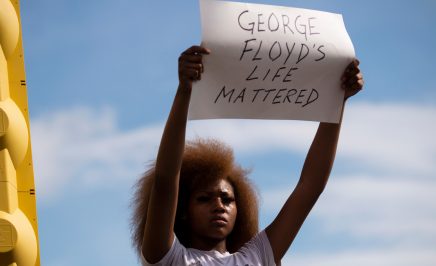 A women in a white t shit hold a sign saying 