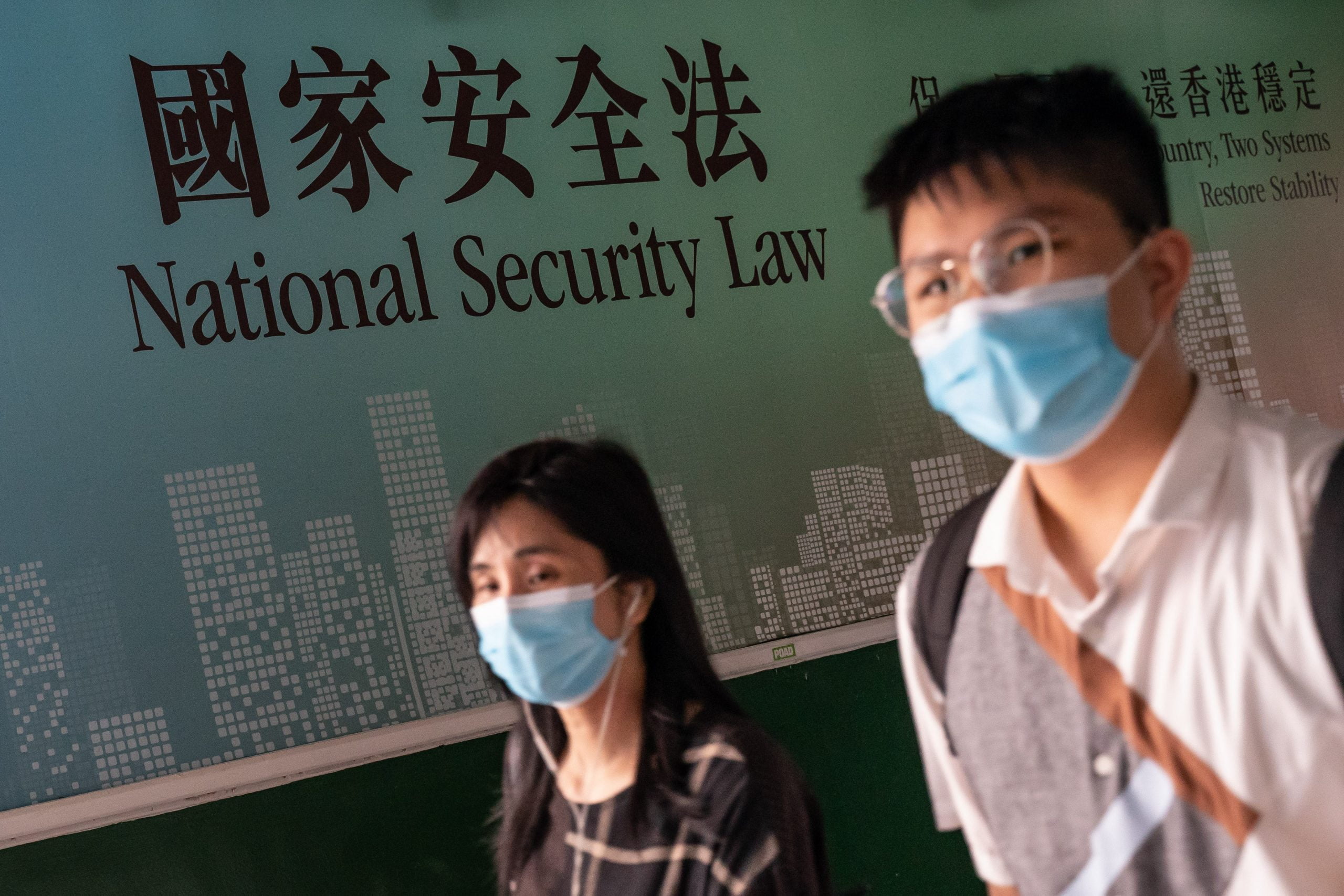 Two people wearing masks walk past a sign that reads "National Security law".
