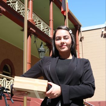 Image of Indigenous Rights activist, Cheree Toka. She's wearing a black blazer, and holding a brown cardboard box full of petition signatures.