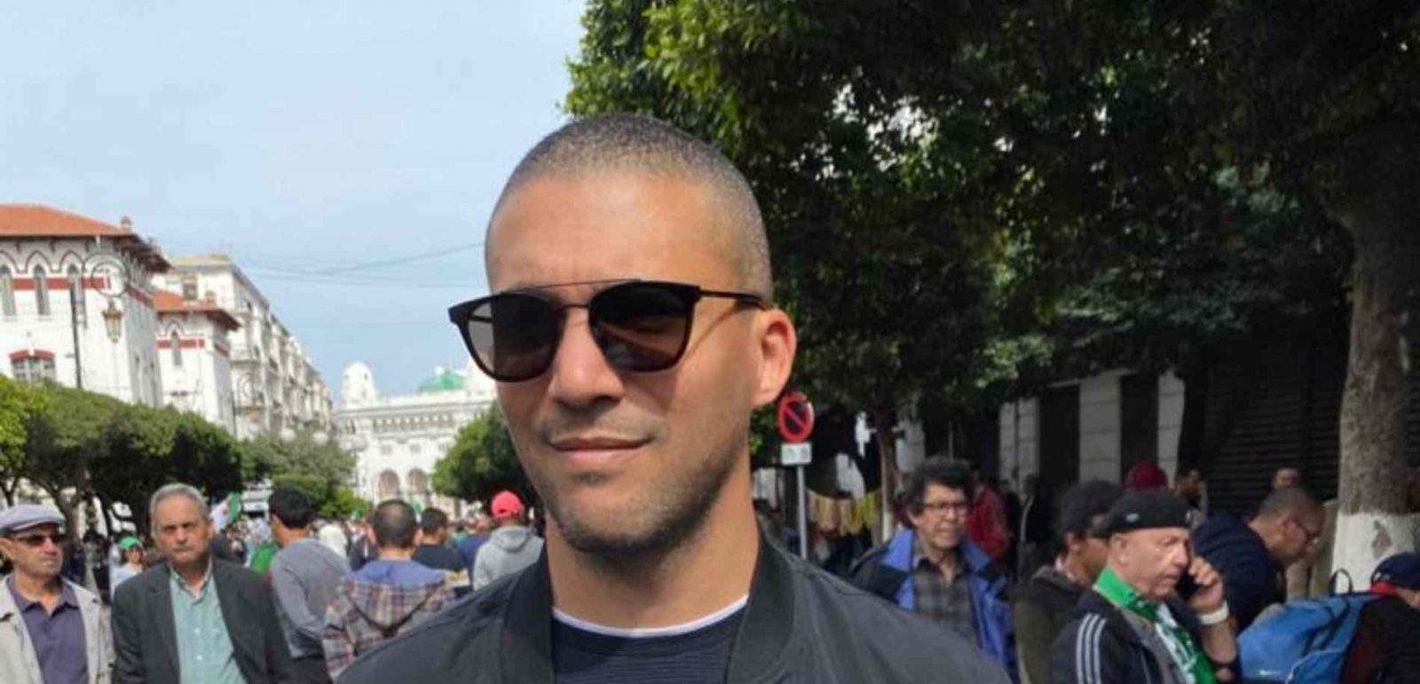 Khaled in dark sunglasses and a grey shirt in front on protesters.