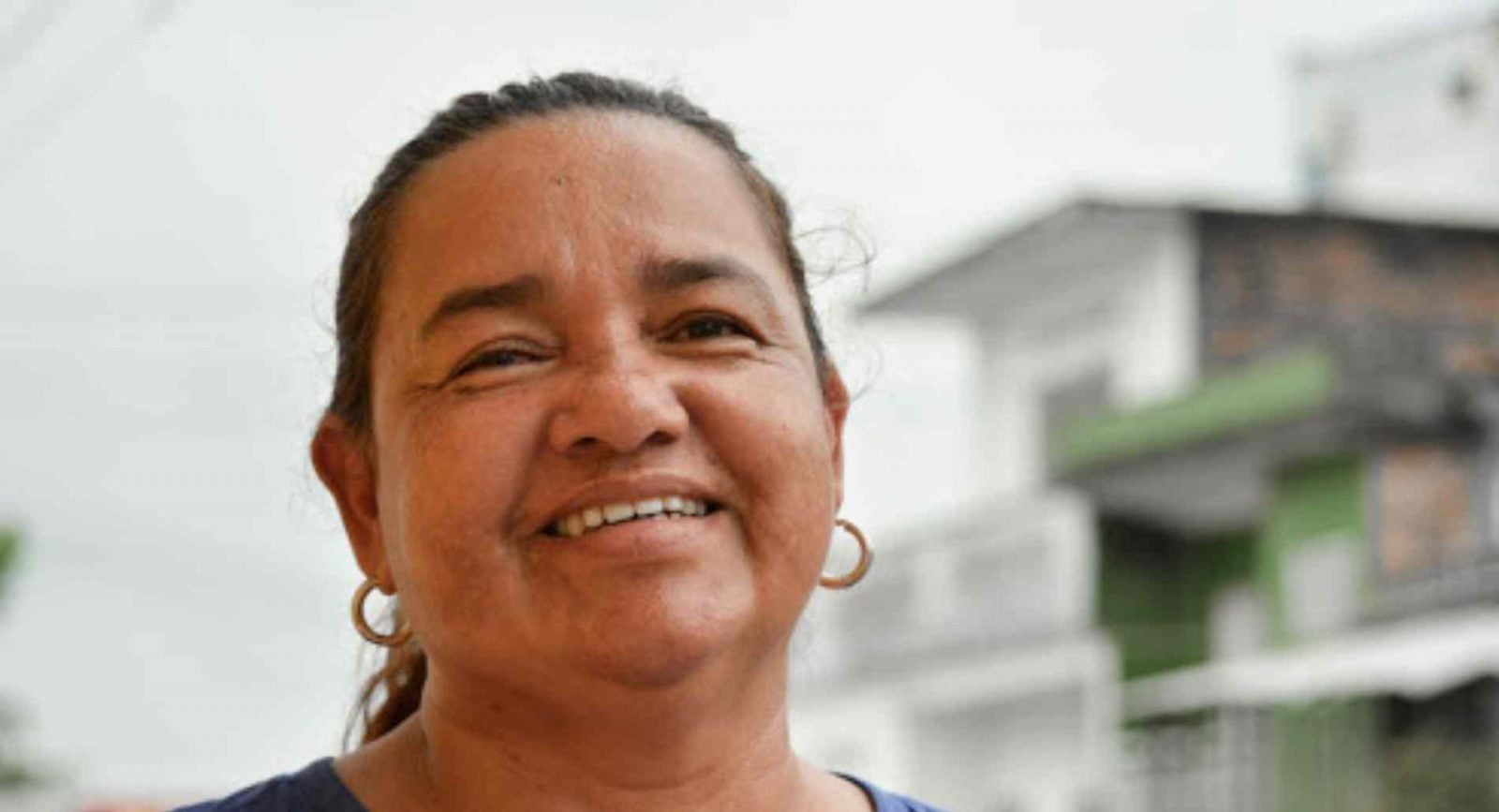 Jani wearing gold earrings smiles in front of a white building.