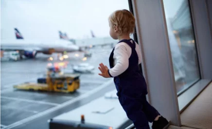 a small child leans on an airport window looking out at planes on the tarmac