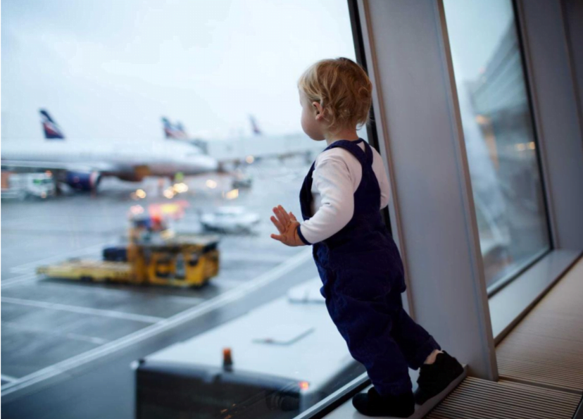 a small child leans on an airport window looking out at planes on the tarmac