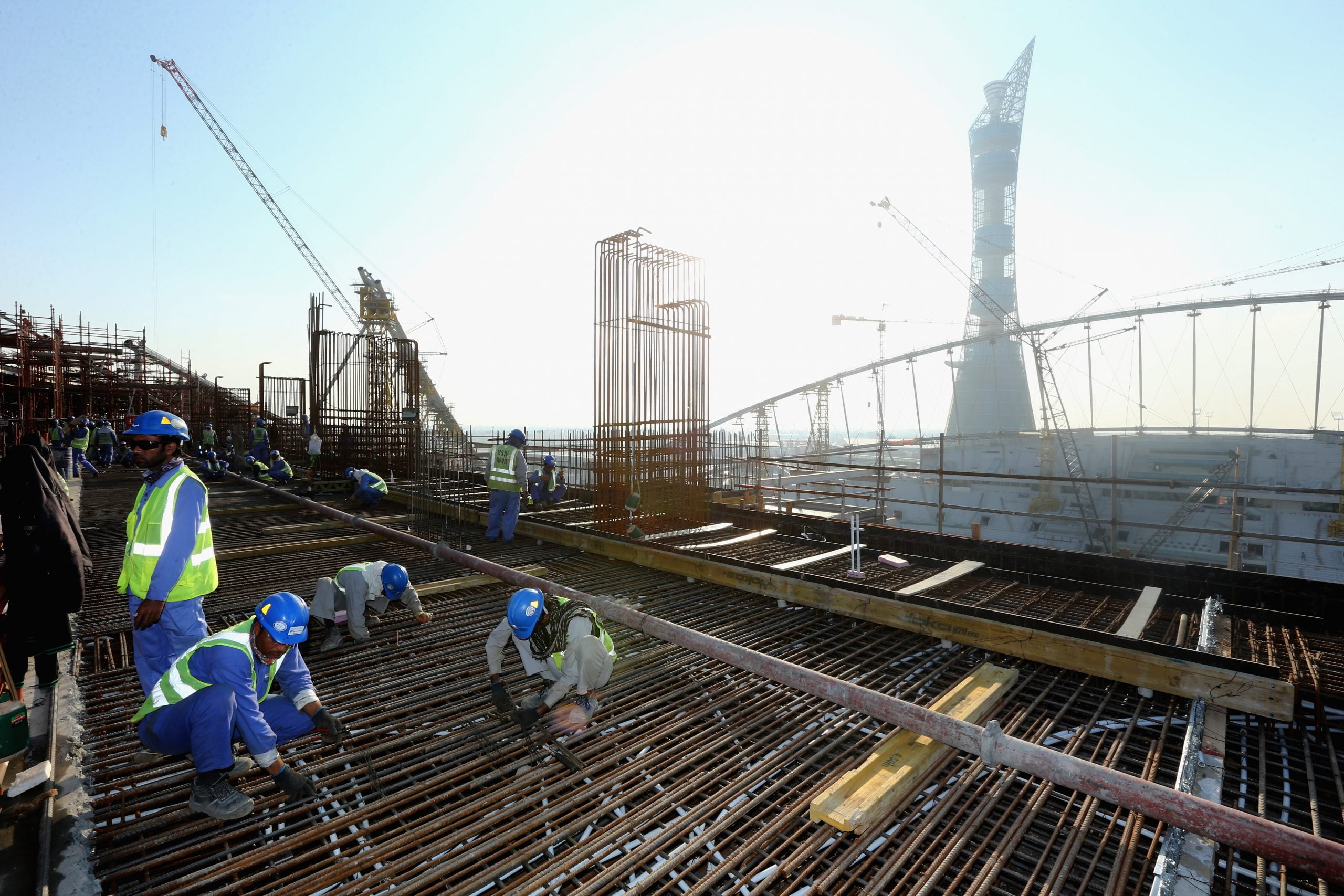 People in blue uniform wearing yellow high vis vests work at a construction site in Qatar, ahead of the FIFA world cup.