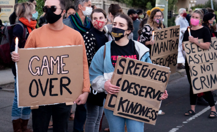activists standing at a rally, wearing masks, holding cardboard signs reading 