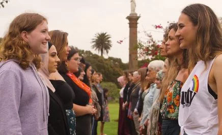 Women and girls gather in 2 lines in a park.