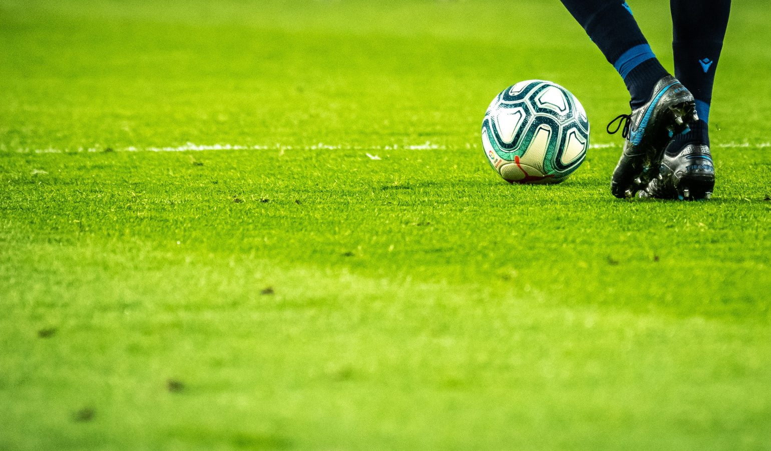 Stock image of a feet level shot of footballer kicking a ball on a pitch