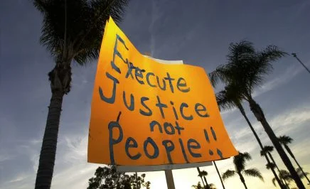 A protester holds a sign up against a backdrop of palm trees which reads 'execute justice not people' during an anti-death penalty protest.
