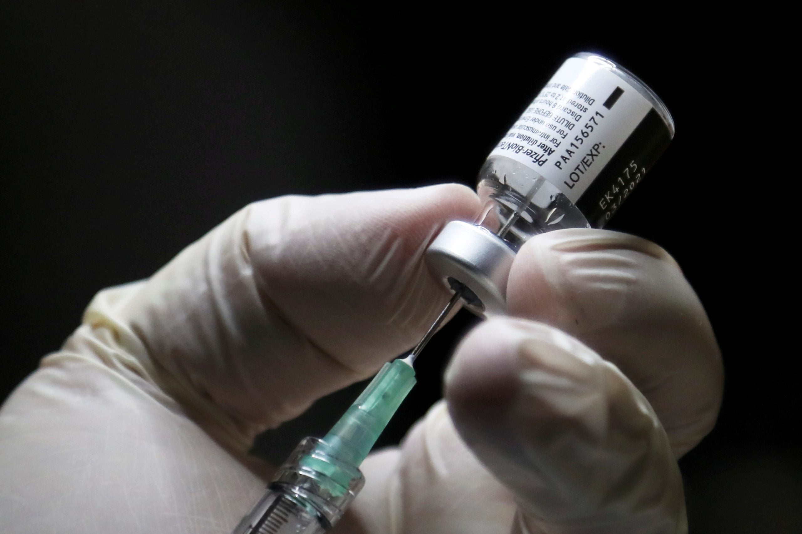 A closeup shot of a healthcare worker's gloved hands preparing to administer a vaccine.
