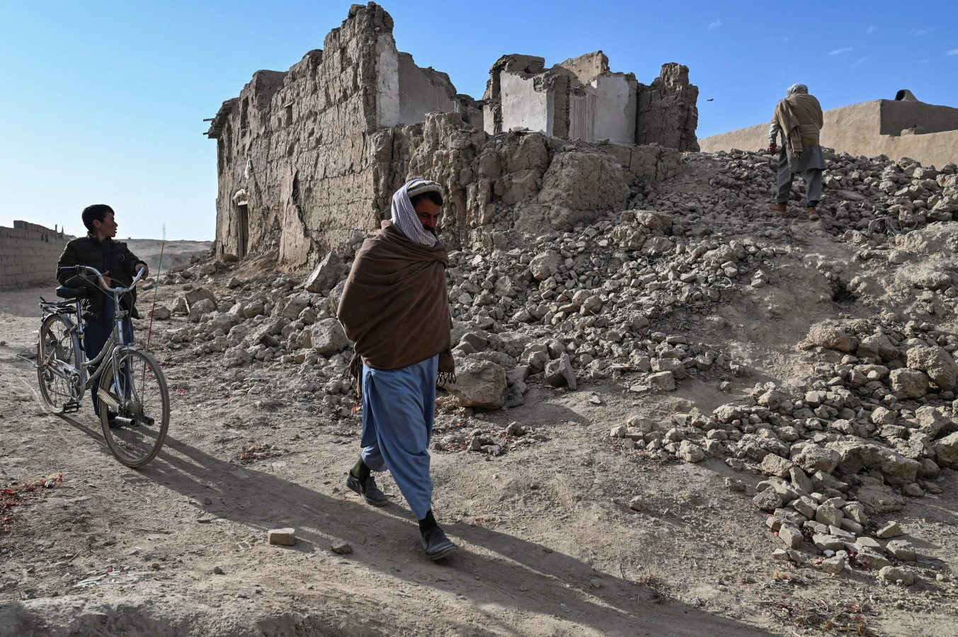 people walk past the ruins of destroyed houses in Arzo village on the outskirts of Ghazni. - Rural areas such as Arzo bore the brunt of the two-decade conflict that saw Taliban insurgents face US, NATO and Afghan forces, with civilian casualties inflicted by both sides.