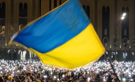 People gather for a rally in support of Ukraine in front of parliament, Ukraine flag waving in the wind is front and centre.