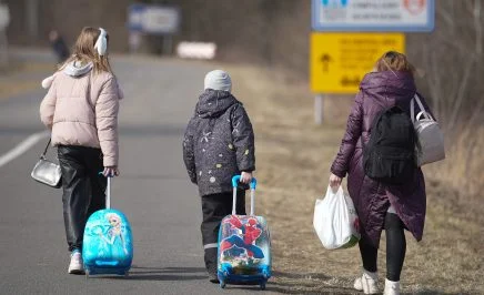 Three young children walking down a road with suitcases.