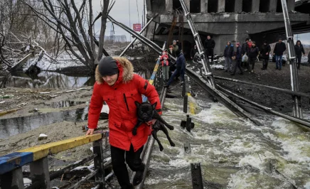 image of a man fleeing war, he's holding his dog while crossing a bridge